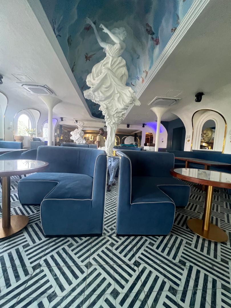 Restaurant interior with curved seating, floral planters, and warm wood finishes